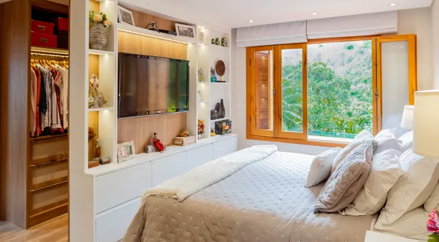 Quarto com estante iluminada, painel de TV e roupeiro embutido