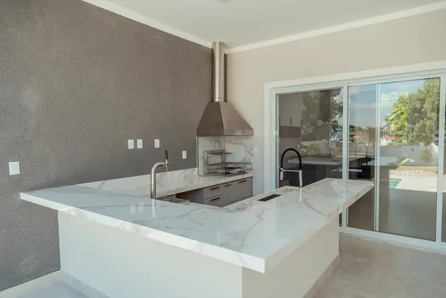 Área gourmet com ilha de pedra, churrasqueira e vista para a piscina