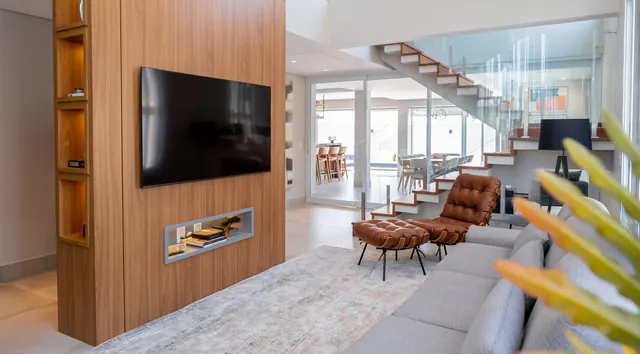 Sala com pé-direito duplo e painel de TV em madeira com nichos iluminados